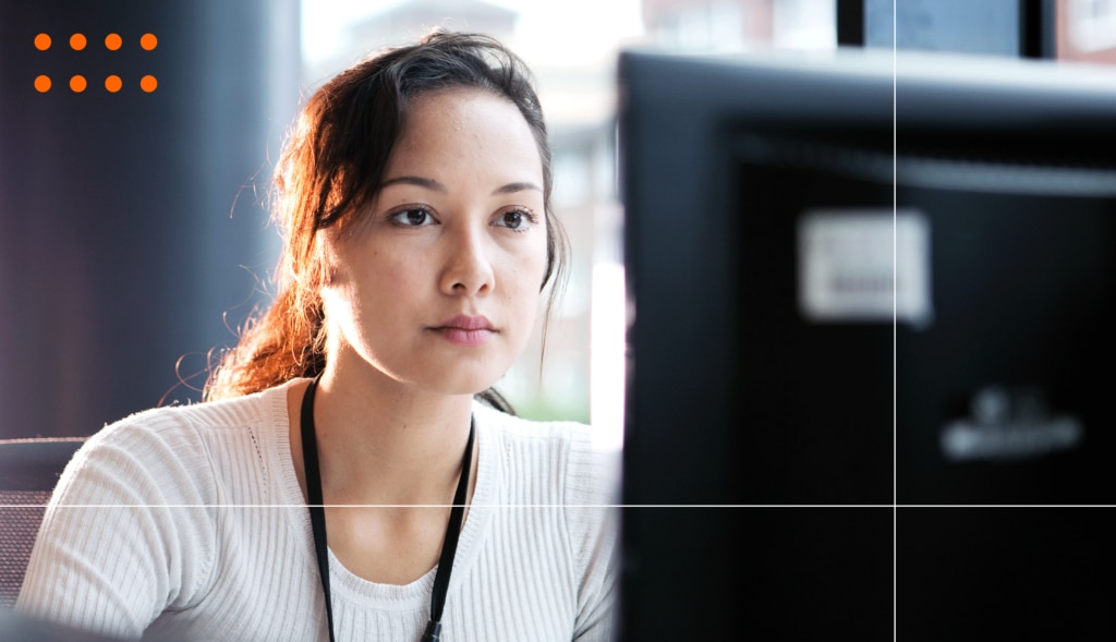 A woman looks at a computer screen, she is wearing a black lanyard