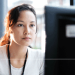 A woman looks at a computer screen, she is wearing a black lanyard