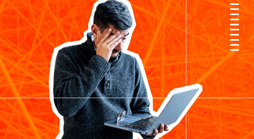 Man with hand to face in despair, holding a laptop.